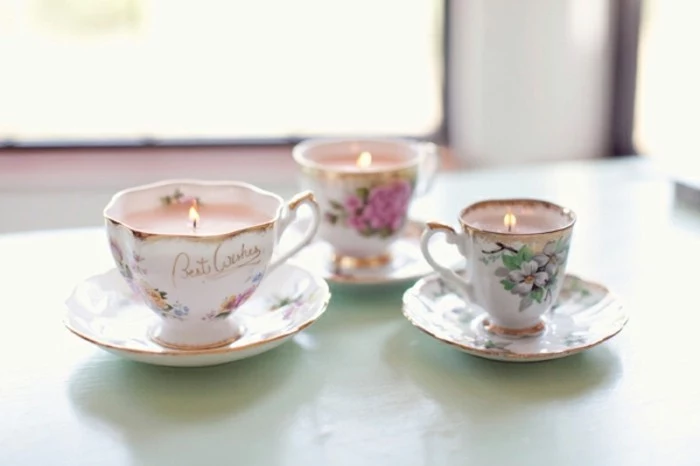 best friend christmas gifts, three painted porcelain cups and saucers, containing lit pink candles, on pale blue surface