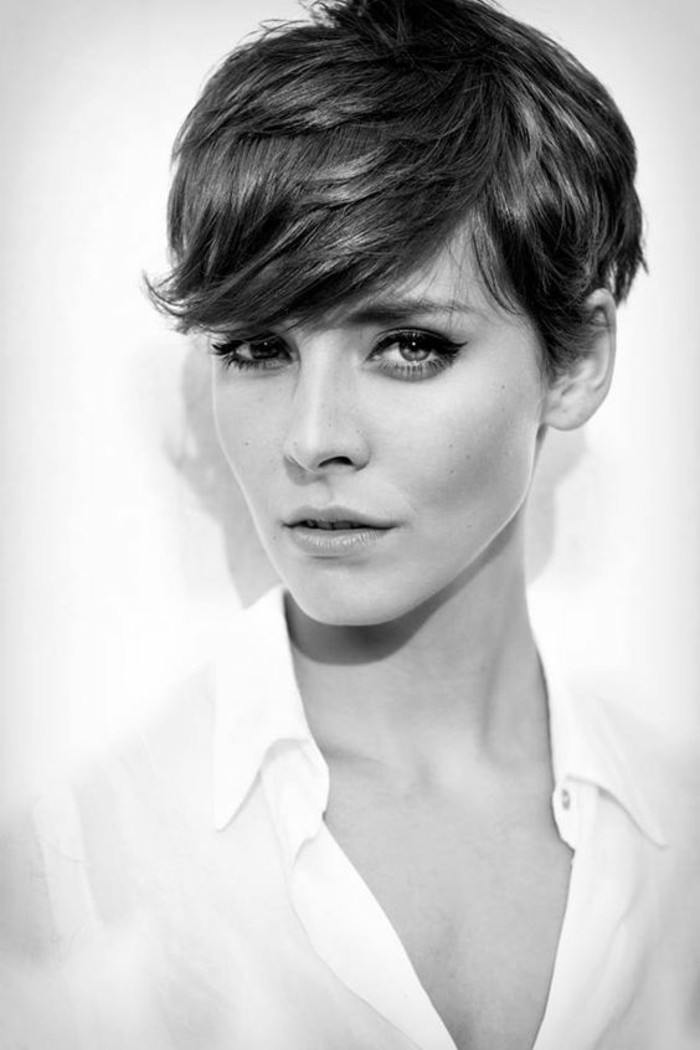 pixie cut, black and white image of woman, with dark layered hair, side bangs above one eye, wearing white shirt and black eyeliner
