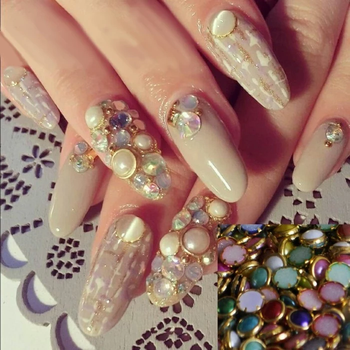rhinestone nail designs, close up of long round nails, two decorated with several multicolored rhinestones, others with gold designs and less rhinestones