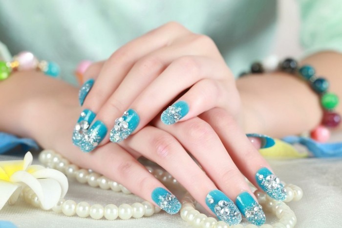 nail designs with rhinestones, two hands with vivid turquoise blue nails, each nail decorated with silver glitter and many rhinestones