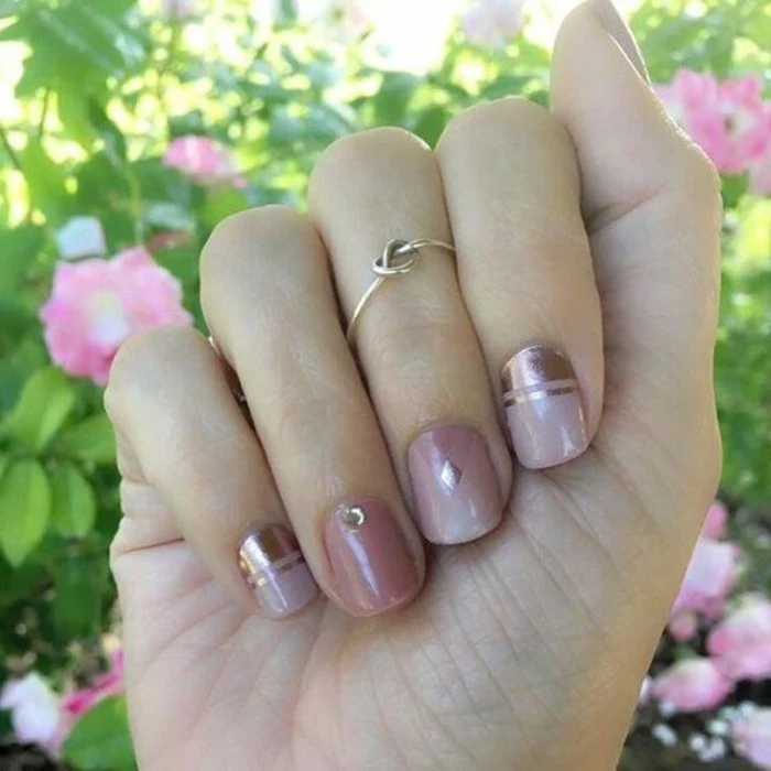 nail designs with rhinestones and glitter, close up of hand with short nails, painted in pastel and metallic pink, decorated with one rhinestone