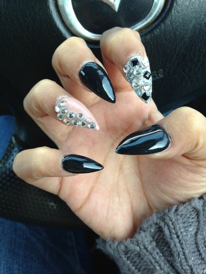 bling nail designs, hand with sharp nails, three painted in shiny black, one in pale pink decorated with rhinestones, one white with silver and black rhinestone details
