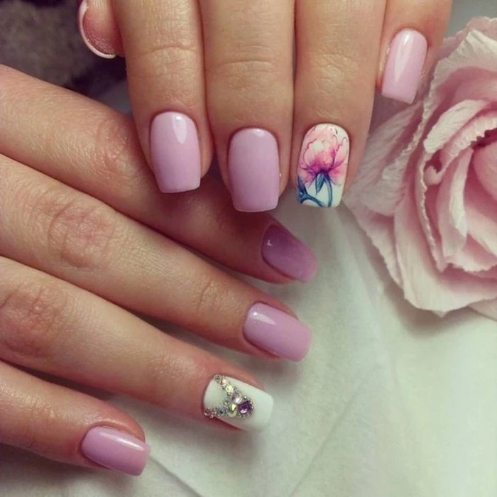 nails with rhinestones, close up of two hands, nails colored in pastel pink and white, one nail has a rhinestone decoration, one nail has a painted rose