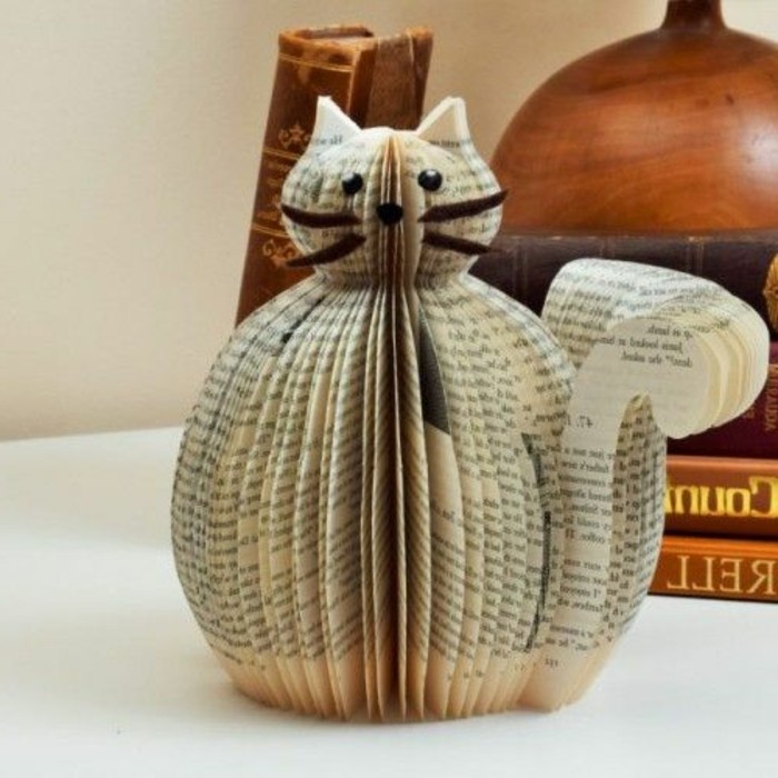 book folding art, cat figure made from cut and folded book pages, decorated with paper eyes and nose, and felt whiskers