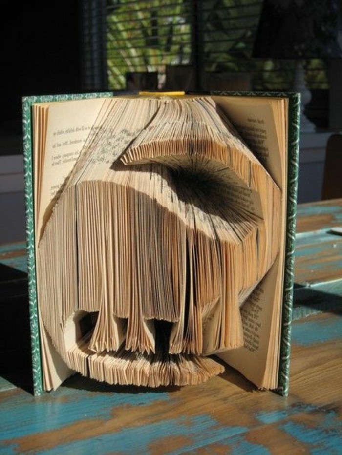 book folding art, a dinosaur shape, made from cut and folded pages, inside a vintage book, with green and white patterned hard covers