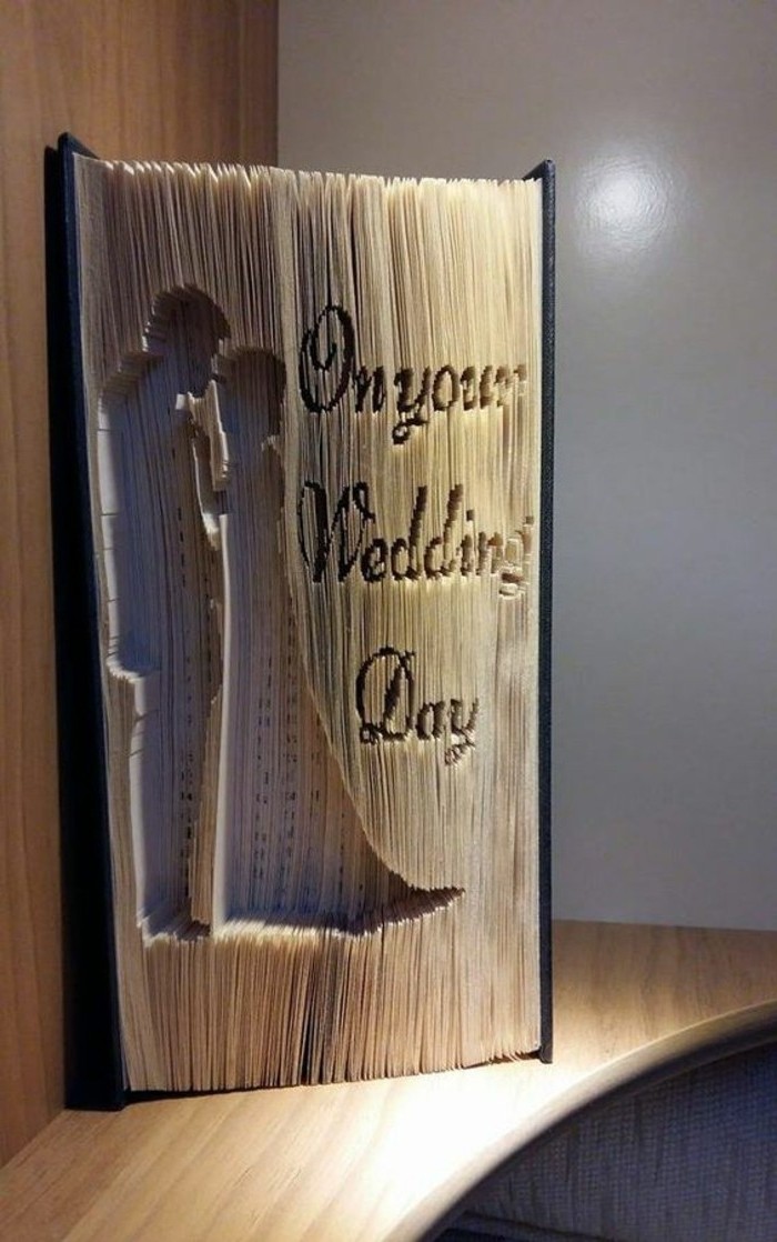 book folding art, closed thick book, with dark hard covers, pages carved with an image of a couple holding hands, and the message on your wedding day
