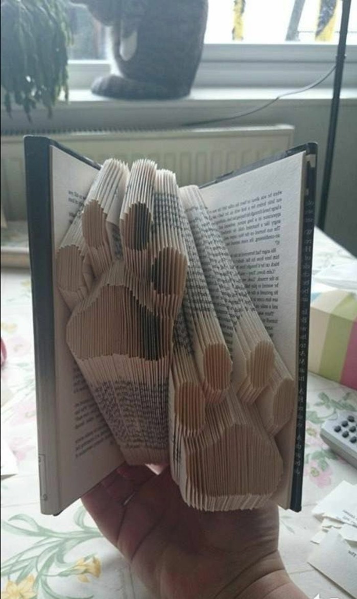 book folding patterns, two paw prints, made from folded pages, inside an open book, with hard dark covers, held by hand