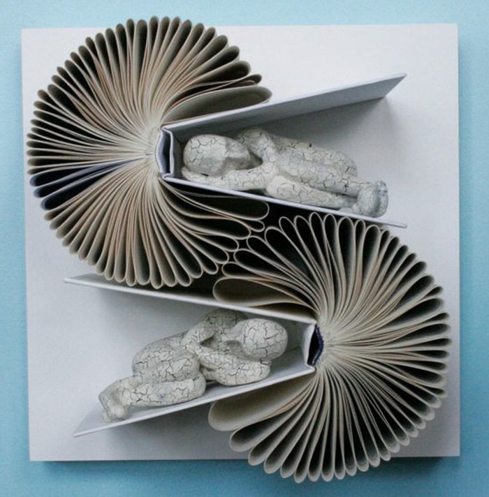 bookfolding, artwork made from two open books, stuck on a canvas, with folded pages, and two human figures made from cracked white stone, placed between the books' covers