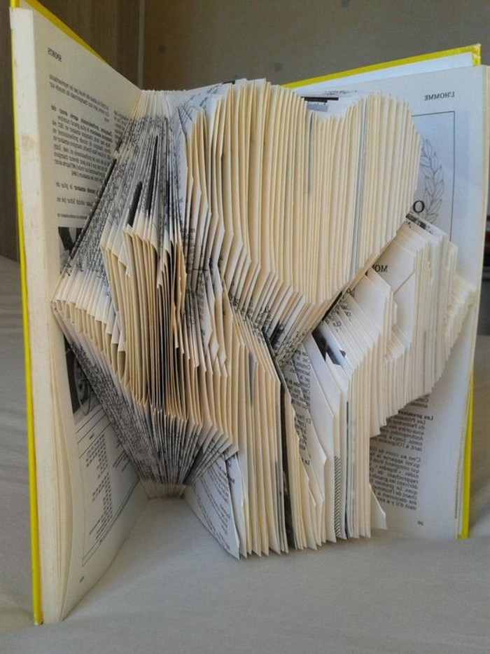 bookfolding, 3D image of two hands, holding a heart shape, made from folded pages, inside an open book, with hard yellow covers