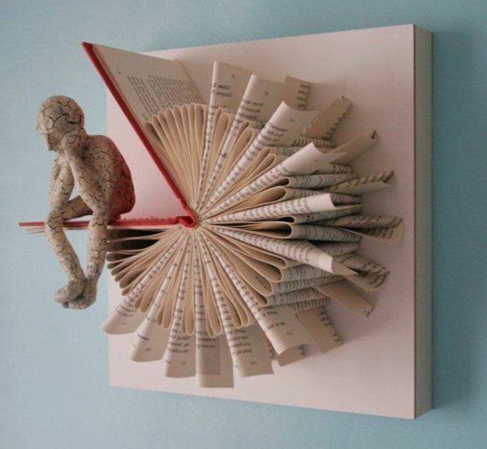 bookfolding, art piece made from an opened book, with hard red covers and folded pages, glued to a canvas, and made to look like a watch, human figure made from white cracked stone, sitting on one cover