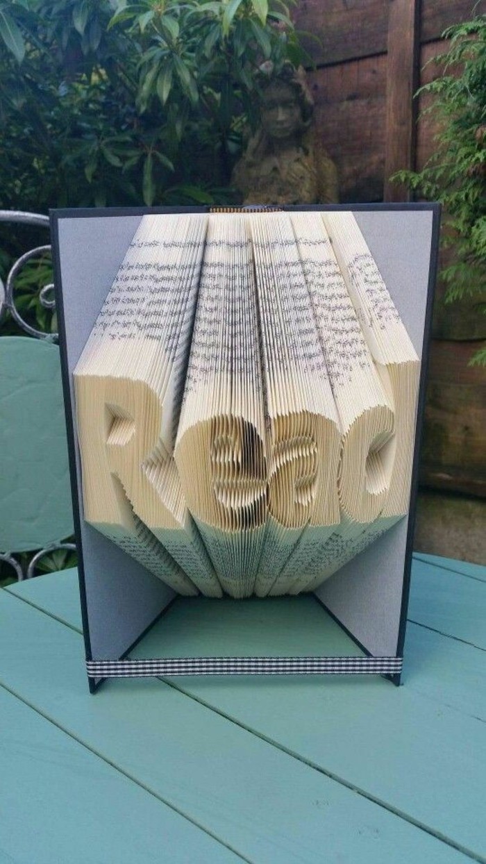 bookfolding, the word read, made from folded pages, inside a book with grey and black hard covers, tied with a chequered ribbon