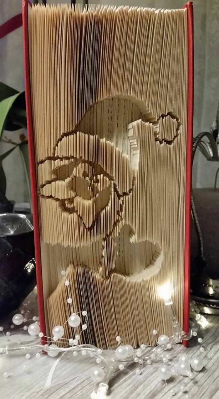 bookfolding, closed thick book, with red hard covers, and a cartoon image of santa claus, carved into its pages