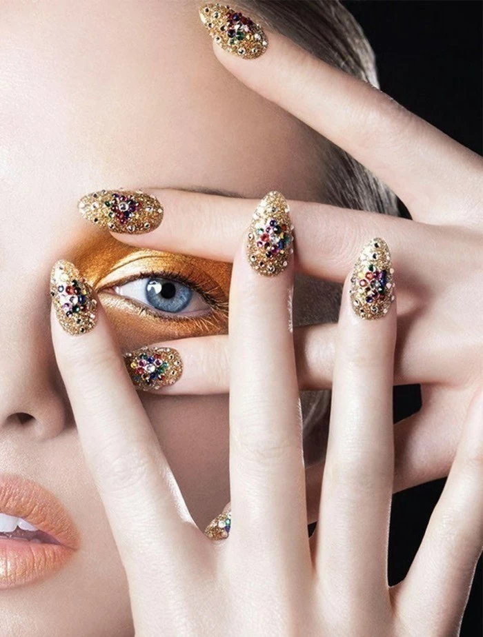 close up of woman's face and fingers, gold eye make-up and golden nails, decorated with multicolored rhinestones
