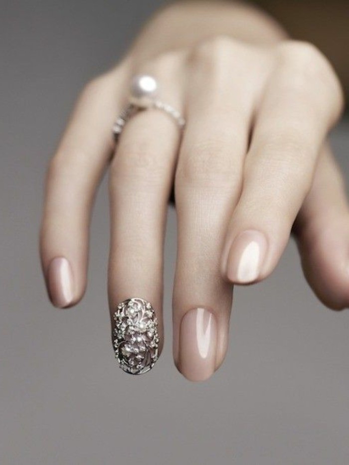 slim hand with long fingers and a pearl ring, fingernails painted in nude polish, one fingernail has decoration with metal details