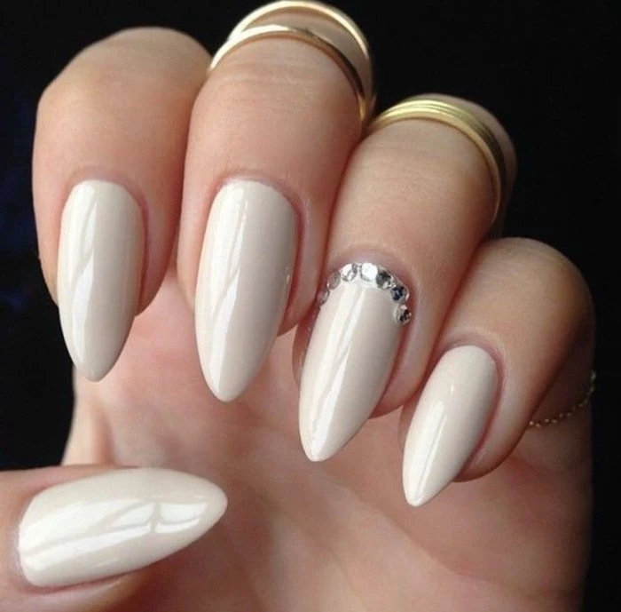 very pale nude nail-polish with rhinestone detail, on hand with several fingers