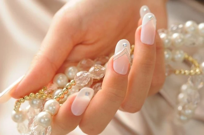 hand holding pearl necklace, pale pink nails with white tips, decorated with white dots and one rhinestone each