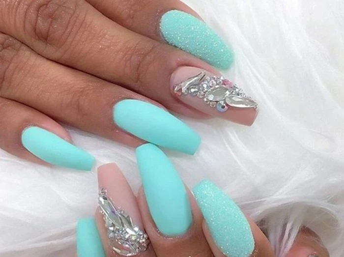 tan hands with long sharp and semi-square nails, turquoise and pink nail polish, white glitter and rhinestone decorations