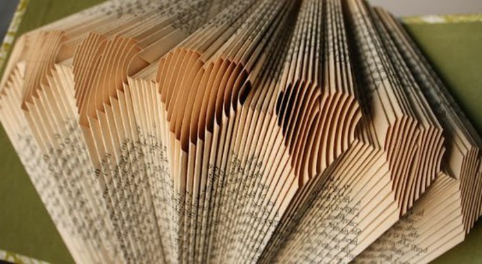 close up of vintage book pages, folded to create heart shapes, green and white covers of a book, are visible in the background