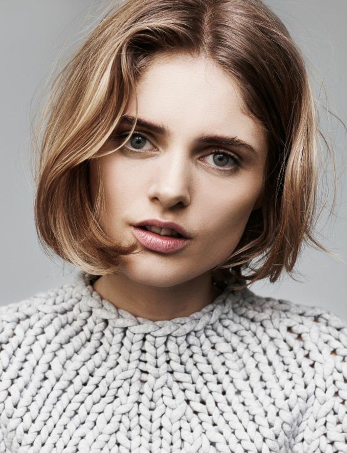 short haircuts, woman with dark blonde wavy bob, parted in the middle, with natural-looking make up and chunky knit grey top