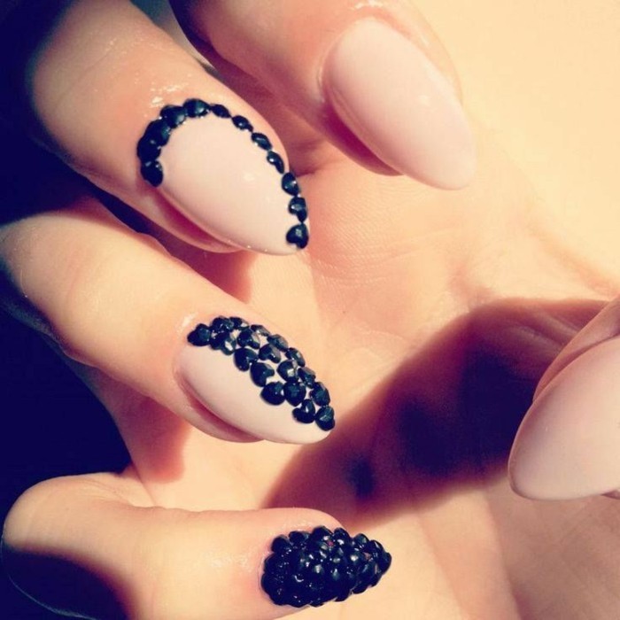 hand with nails painted in nude polish, decorated with black rhinestones, pinkie finger's nail covered in black rhinestones