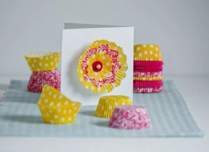 easy kids crafts, flower made from muffin moulds, pinned on a white card, many yellow and pink patterned muffin moulds, stacked together and loosely placed on table