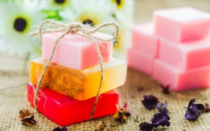 gifts for best friends, three handmade soaps in red, orange and pink, tied with a simple string, flower petals and more pink soaps in background