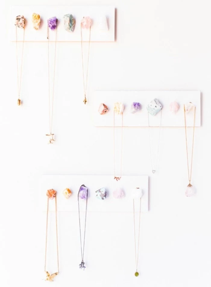 diy gifts for friends, three necklace holders, made from white wooden boards, decorated with colorful stones, several necklaces hanging from the stones