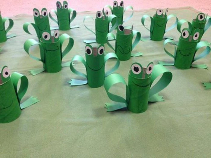many green frogs, made from hand-painted toilet rolls, decorated with green, white and black paper cutouts