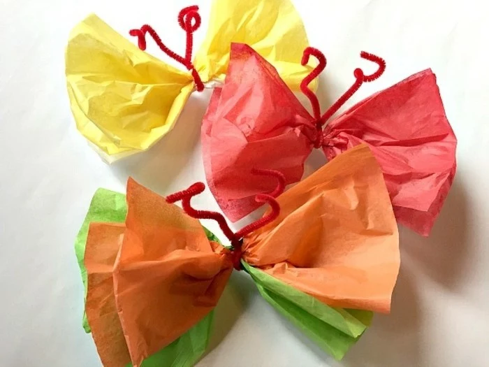 diy art projects, three butterflies made from crepe paper, in yellow and red, orange and green, tied with simple red fuzzy wire