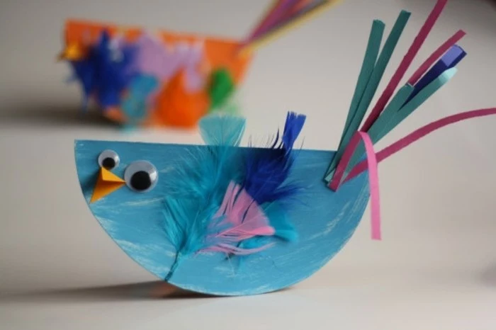 diy art projects, small handprinted blue bird, made of paper, decorated with blue and pink feathers, paper strips and googly eyes