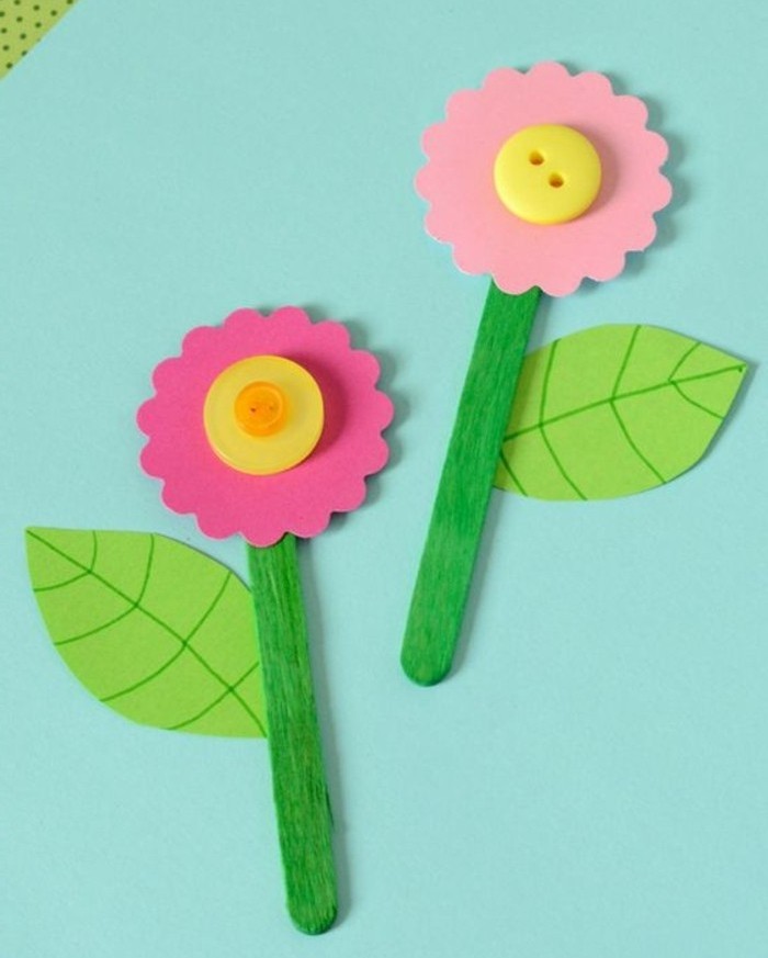 craft ideas for kids, two flowers made from pink felt, yellow buttons and green paper leaves, attached to ice cream sticks painted in green