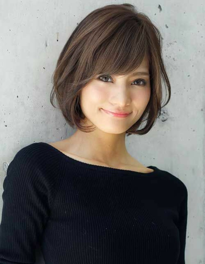 smiling asian woman, with short brown hair and side bangs, wearing black jumper, and pale pink lipstick