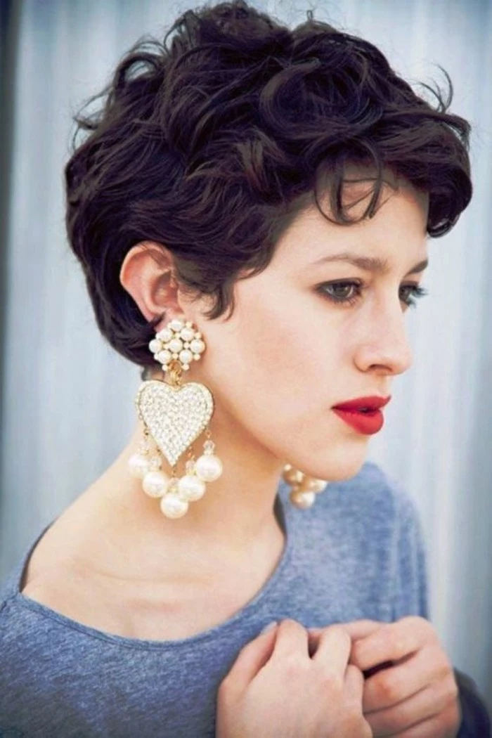 haircuts for women, close up of a woman with very short, dark brown curly hair, grey top and big, heart-shaped earrings with pearls