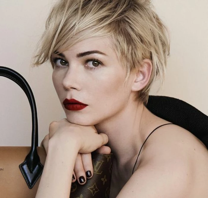 pixie cut, michele williams with short, side-swept blond hair, wearing bright red lipstick, and black nail polish