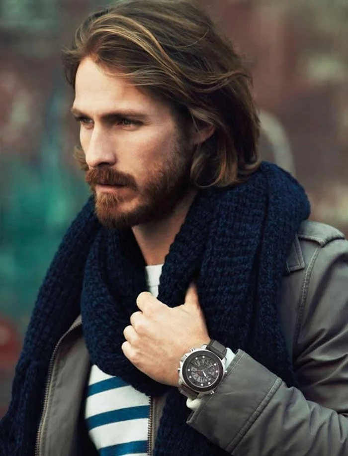 shoulder length hair, dirty blonde man with beard and mustache, wearing khaki jacket and blue chunky knit scarf