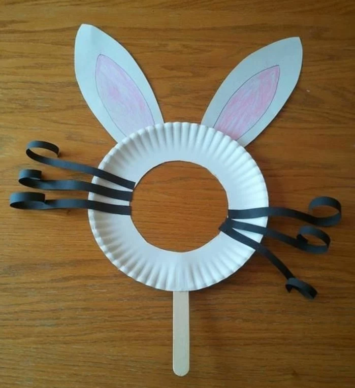 easy kids crafts, bunny mask made from white paper plate with face hole, decorated with black paper whiskers, and white hand-decorated paper ears