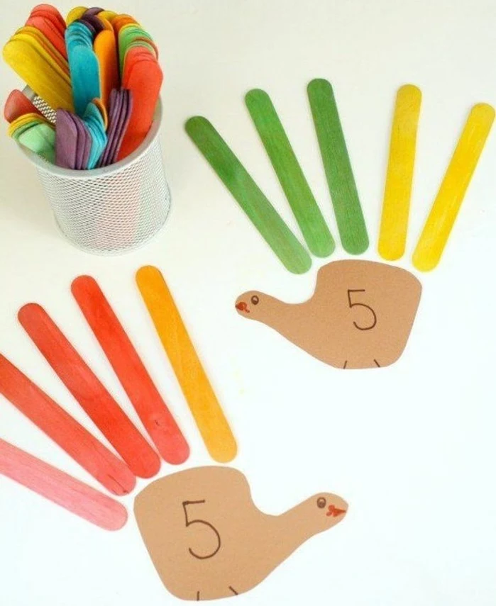 two turkeys made from brown paper shapes, and colorful ice cream sticks, pencil holder containing more ice cream sticks in different colors nearby