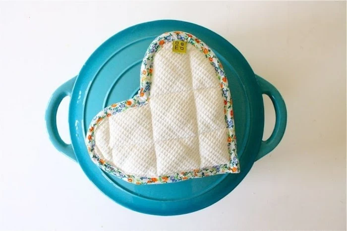 diy gifts for friends, handmade pot holder shaped like a heart, made from white fabric with floral trim, placed on a turquoise pot with handles