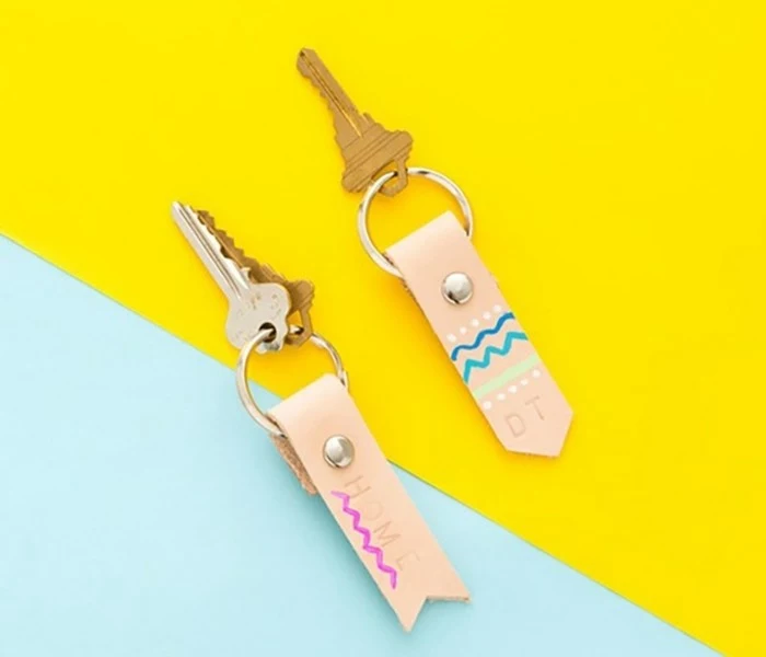 diy gifts for friends, two sets of keys, with handmade leather keyrings, in pale pink and decorated with gold studs, and pink and blue scribbles