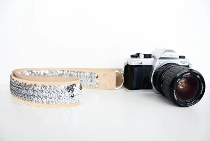 diy gifts for friends, black and silver retro camera, attached to a cream colored leather neck strap, hand-decorated with silver sequins