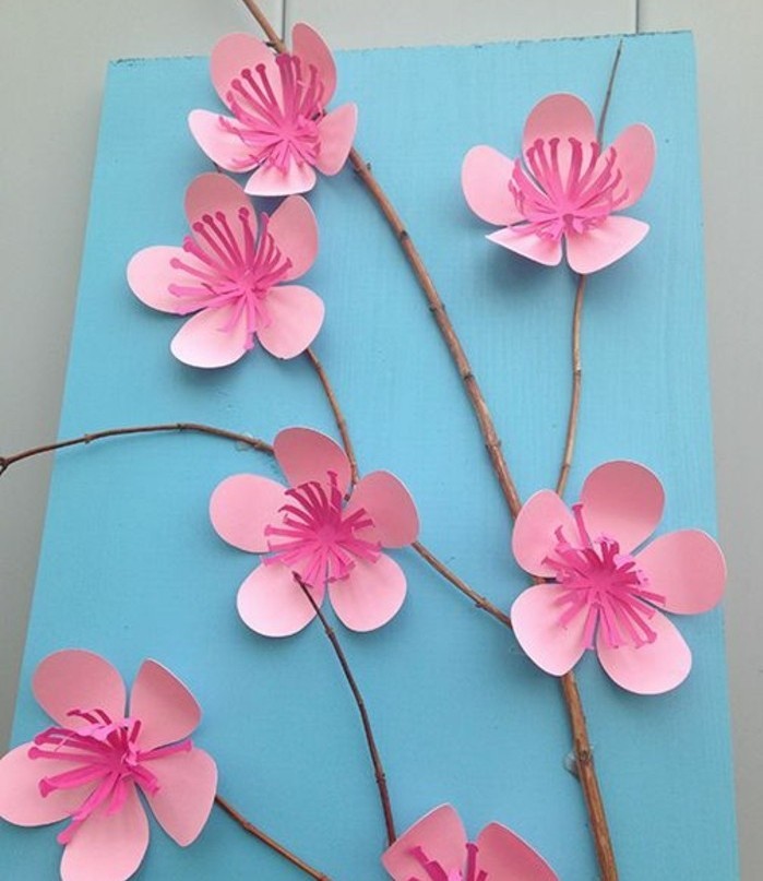 diy projects for kids, small twig decorated with cherry blossoms, made from paper in two shades of pink, on a pale blue background
