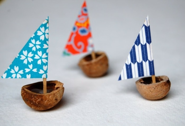 easy kids crafts, three little boats made from walnut shells, decorated with colorful triangular crepe paper sails on toothpicks