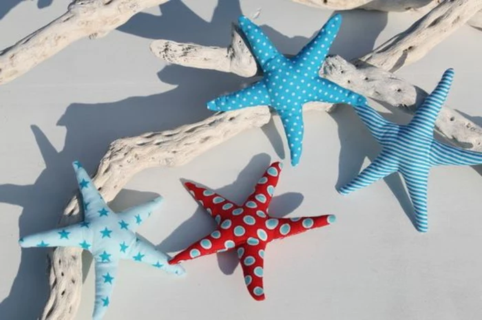 summer craft ideas, four stuffed starfish, made from blue and red patterned fabric, placed over white-painted driftwood