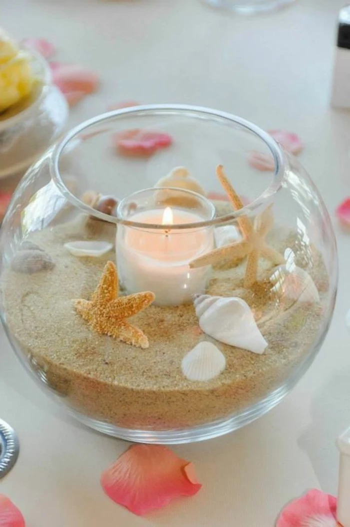 summer crafts for adults, round glass bowl, half-filled with sand, various seashells and dried starfish, containing one lit candle in glass holder