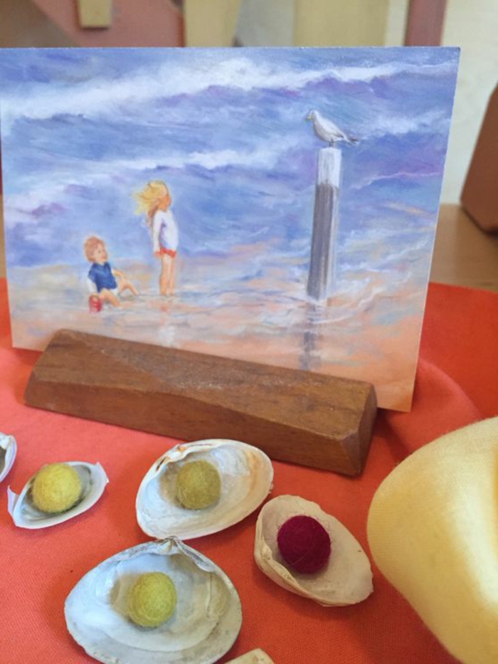 summer crafts for adults, several seashells containing small, round fabric decorations in yellow and red, near a painting of two children, looking at a seagull