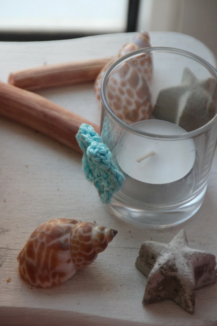 diys to do with friends, small glass decorated with teal knitted star, containing one tiny candle, seashells and starfish nearby
