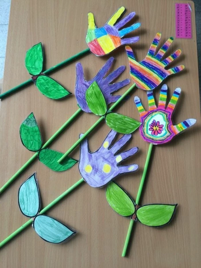 five flowers made from hand-painted hand-shaped cutouts, in different colors, with green straw stalks and paper leaves