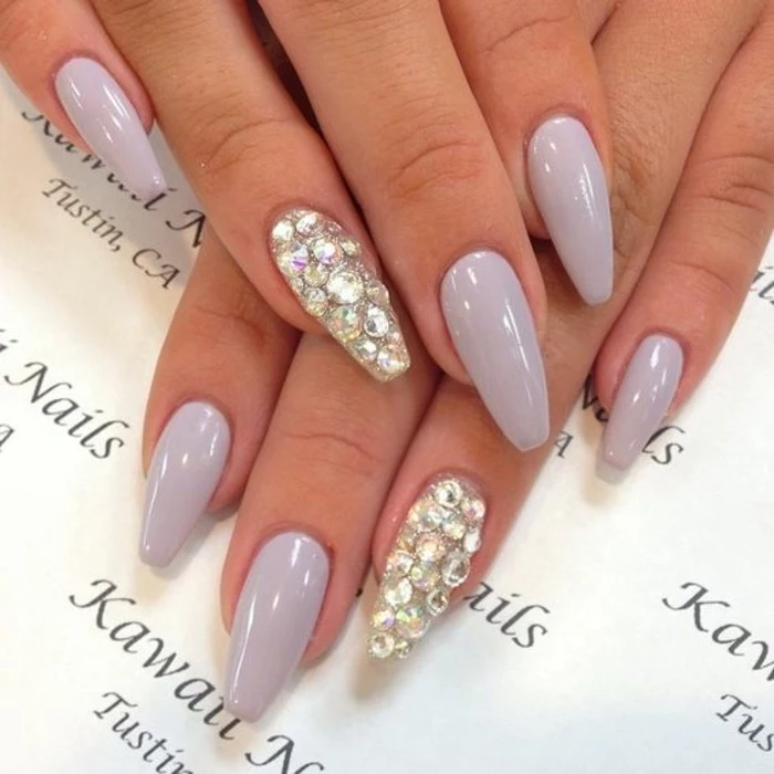 two hands with very pale lilac nail polish, ring fingers' nails entirely covered in rhinestones