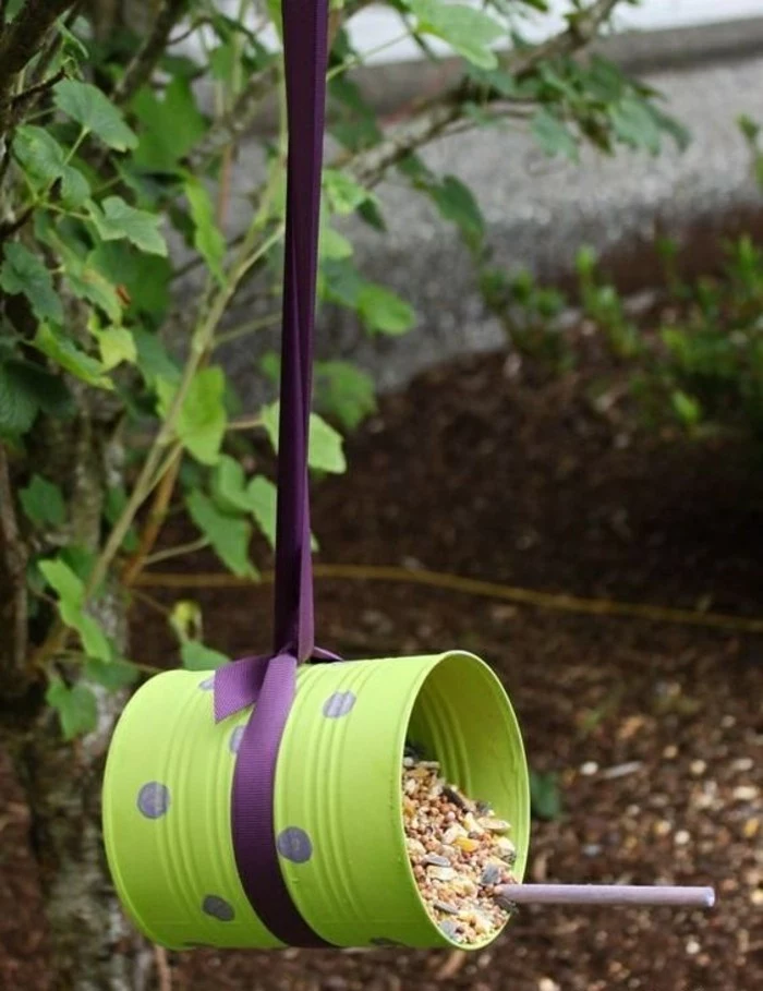 tin can projects, bird feeder made from tin can painted green, with purple polka dots, containing lots of different seeds, hanging on a purple ribbon