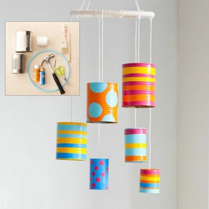 decoration made from six cans in different colors, decorated with paint in different colors, with shapes and stripes, hanging on white thread